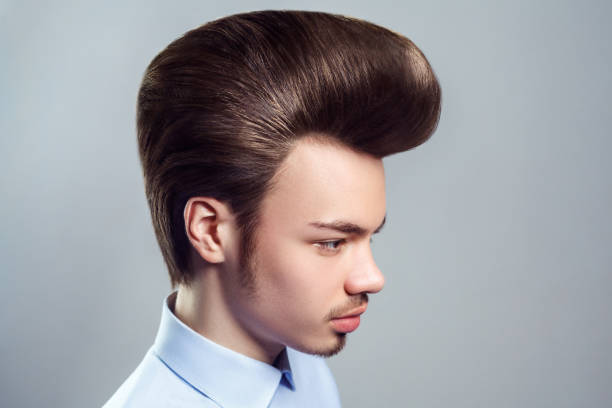 Young adult man with mustache and beard with retro classic pompadour hairstyle, looking away. Side view portrait of young adult attractive man with mustache and beard with retro classic pompadour hairstyle, looking away with serious expression. Indoor studio shot isolated on gray background. rockabilly hair men stock pictures, royalty-free photos & images