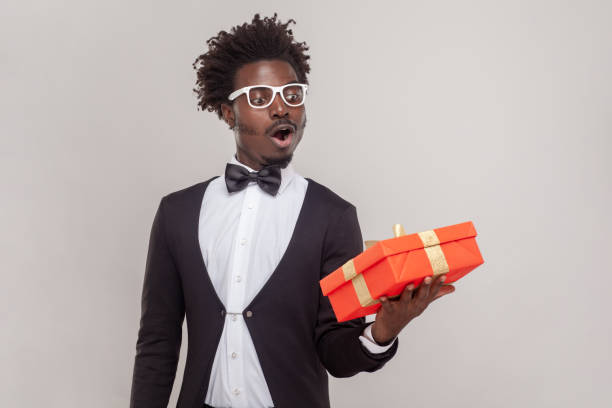 istock Surprised astonished man in glasses standing with red gift box, looking at present with open mouth. 1484904469