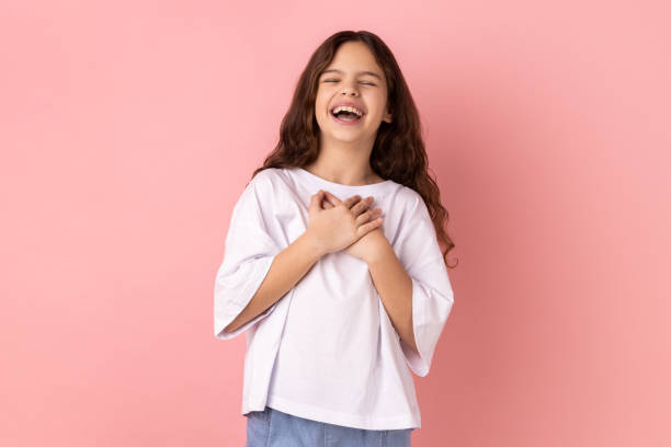 Little girl hearing funny joke, laughing out loud, holding belly, expressing positive emotions. Portrait of crazy optimistic little girl wearing white T-shirt hearing funny joke, laughing out loud, holding belly, expressing positive emotions. Indoor studio shot isolated on pink background. child laughing hysterically stock pictures, royalty-free photos & images