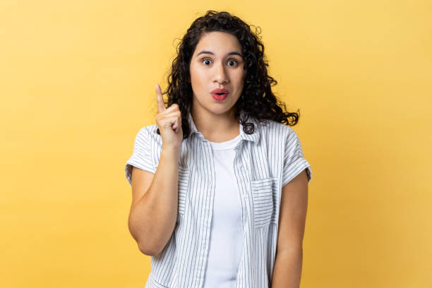 istock Woman pointing upwards, looking at camera with open mouth, having new great idea. 1484905633