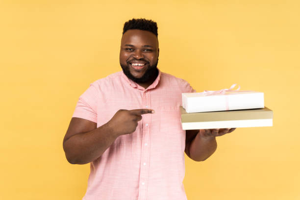 istock Man holding and pointing at gift boxes, looking at camera with happy smile. 1484905750