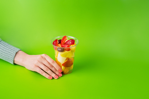 Fruit salad in a plastic cup on green background