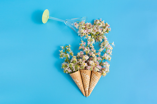 Three sweet crispy wafer cups with chestnut flowers on a blue background. Chestnut petals pour out of a martini glass.