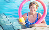 Senior women (over age of 50) in sport goggles, swimsuit, with swim noodles in swimming pool before water aerobics.