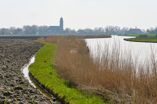 Panorama of a typical Dutch polder landscape with a curved ditch in between flat grassy meadows under a nicely cloudy sky.