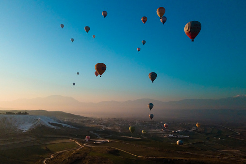 Hot air balloons flying over Pamukkale valley against rising sun over mountains. Aerial drone photo