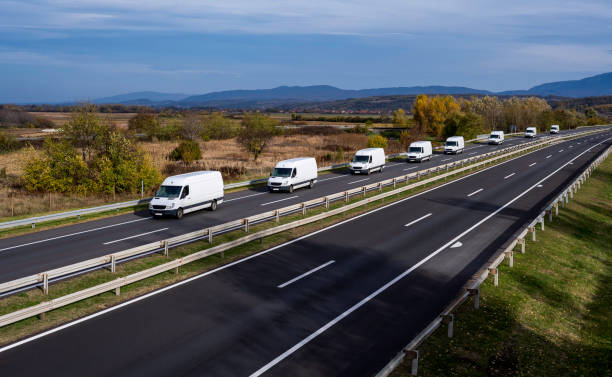 ocho minivans blancas se mueven en un convoy en la carretera. van de reparto blanca en la carretera. blanco moderno entrega pequeña carga carga furgoneta de mensajería que se mueve rápido en la carretera de la autopista al suburbio urbano de la ciudad. - convoy fotografías e imágenes de stock