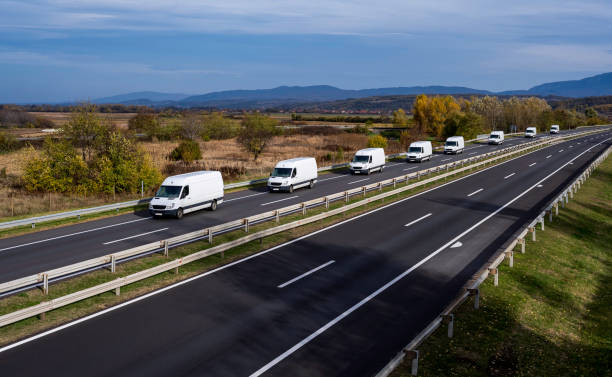 Eight white minivans are moving in a convoy on the highway. White delivery van on the highway. White modern delivery small shipment cargo courier van moving fast on motorway road to city urban suburb. Eight white minivans are moving in a convoy on the highway. White delivery van on the highway. White modern delivery small shipment cargo courier van moving fast on motorway road to city urban suburb. convoy stock pictures, royalty-free photos & images