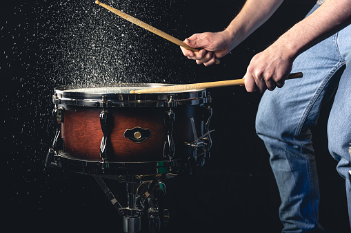 Drummer using drum sticks hitting snare drum with splashing water on black background.