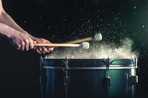 A man plays a musical percussion instrument with sticks close-up on a black background, a musical concept with a snare drum, beautiful stage lighting.