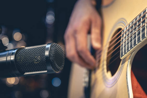 istock Male musician playing acoustic guitar behind microphone in recording studio. 1484921012