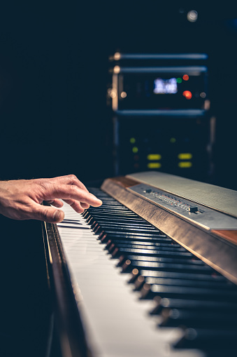 Male hand playing piano keys in dark music studio interior, recording studio concept.