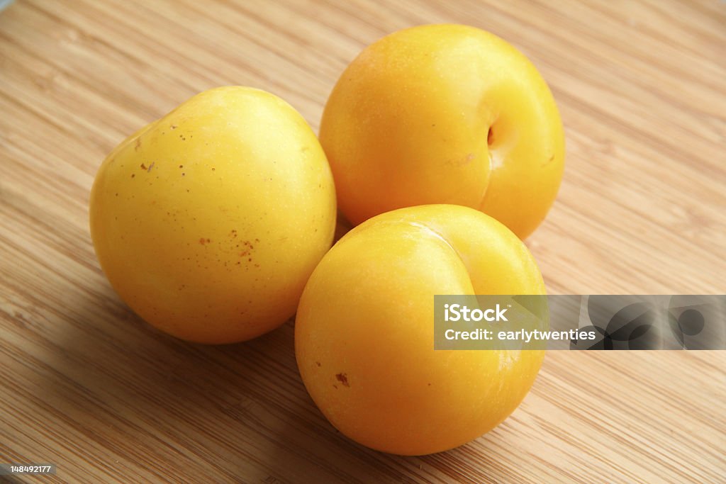 Yellow Plums Three juicy yellow plums against a wooden background Berry Fruit Stock Photo