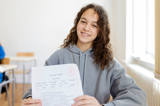 Portrait of teenage girl sitting in classroom with perfect grade a plus test results. Childhood, education and people concept