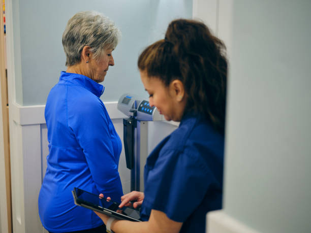 krankenschwester in einer arztpraxis, die einen älteren patienten wiegt - dieting weight scale doctor patient stock-fotos und bilder