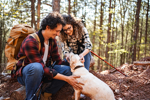 Young adventurous couple petting their white dog while on a hike