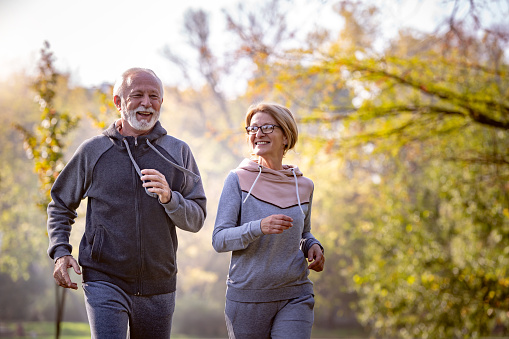 Cheerful active senior couple jogging in the park. Exercise together to stop aging.