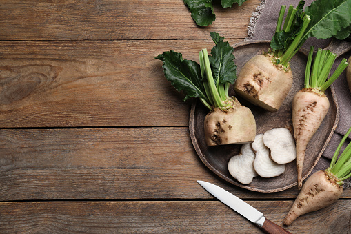 Whole and cut sugar beets on wooden table, flat lay. Space for text