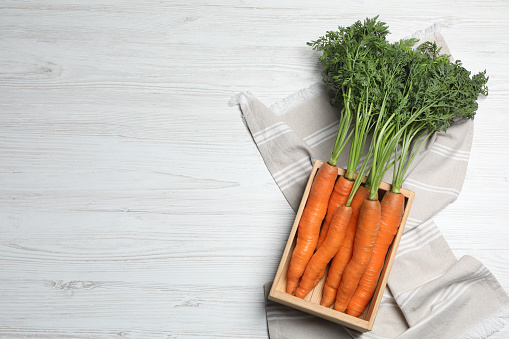 Fresh carrots in crate on white wooden table, top view. Space for text