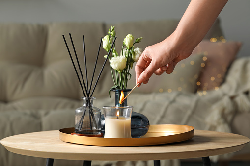 Woman lighting candle at wooden table in living room, closeup