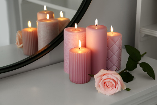 Burning candles and rose on white console table near mirror