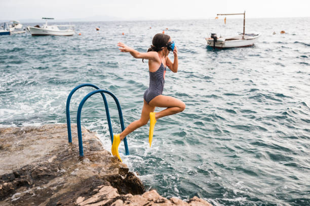 Young girl having fun jumping from a cliff into the sea