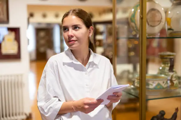 Photo of Young female looking at exposition of antique ceramic at museum