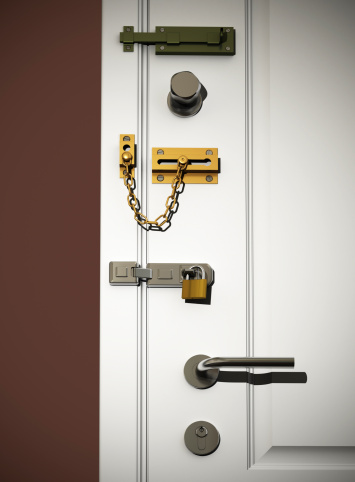 Low angle view on white classic door with several types of DIY safety locks. Scene is lit with a spotlight with small spread for vignetting effect.