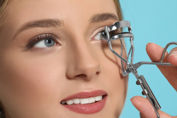 istock Young woman using eyelash curler on light blue background, closeup 1484947677
