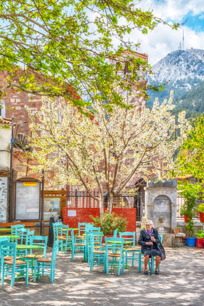 Under the beautiful spring sunlight, a senior woman is sitting in one of the chairs of the old coffee house in the square of the village of Agiasos stock photo