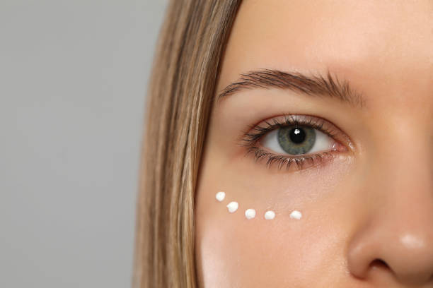 istock Young woman with cream around eye on light grey background, closeup. Space for text 1484947871