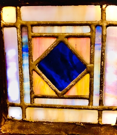 A corner section of a stained glass window with pastel colors including pink, blue, yellow, lavender, and cream inside a Hoboken, New Jersey church.