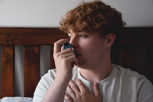 Closeup young man using inhaler for asthma attack