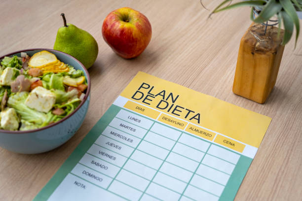 Glowing light bulb in mid-air over the blank checklist with measurement tape and apple on a wooden shelf against green wall with copy space.\nDieting concept.