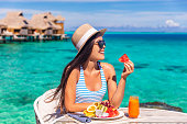 Luxury resort vacation woman eating fruits detox breakfast on beach hotel room with private terrace. Tourist girl healthy diet lifestyle.