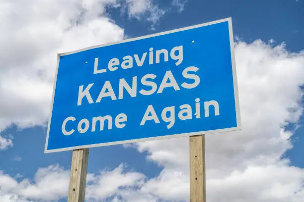 Leaving Kansas, come again - roadside sign at highway against cloudy sky