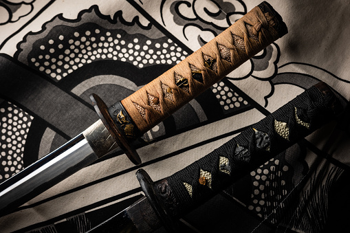 A close up of two traditional Japanese Katana sword handles. The brown one is a real antique with proper materials where as the black handle one is a modern cheap replica.