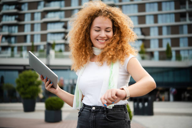 istock Portrait of a beautiful redhead young woman checking the time and using tablet while walking 1484959164