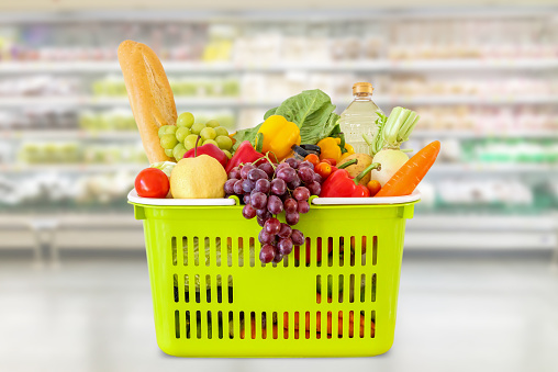 Shopping basket with fruits and vegetables in supermarket grocery store blurred background
