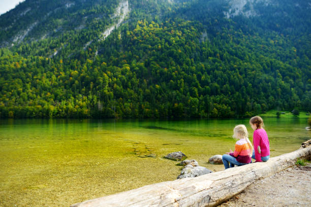 две милые сестры наслаждаются видом на глубокие зеленые воды кёнигзее, известного как самое глубокое и чистое озеро германии, расположенно - konigsee стоковые фото и изображения