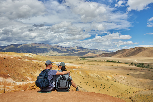 couple of tourists sit with their backs to camera against backdrop of landscape on summer day. Sights of Russia, Siberia and Altai Republic, mars. Tourism and travel. Kosh-agach, Chagan-Uzun