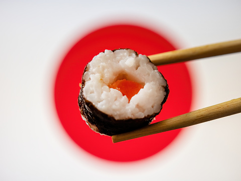 A single spicy tuna sushi roll held in a pair of chop sticks.