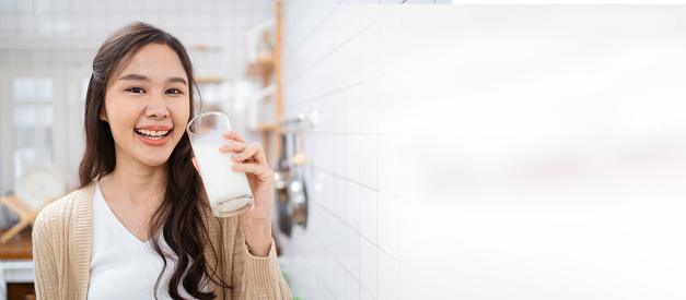 Beautiful happy Asian woman drinking a milk in morning in kitchen and smiling to camera. Happy Asian woman shows a glass of milk and smiles.