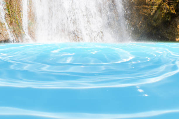Beautiful waterfall in forestry with blue water with ripples on the surface. Blurred transparent blue colored clear calm water surface texture with splashes and bubbles. Water waves with shining.