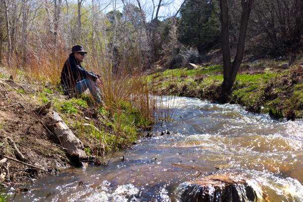 istock Senior Man in Black Hat Sitting on Riverbank 1484979130