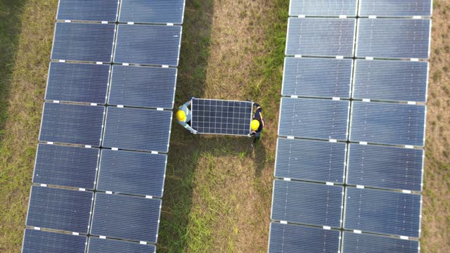Top view of worker holding a Solar Panels and walking in solar farm. engineers inspects construction of solar cell panel. Drone flight fly over solar panels field renewable green alternative energy.