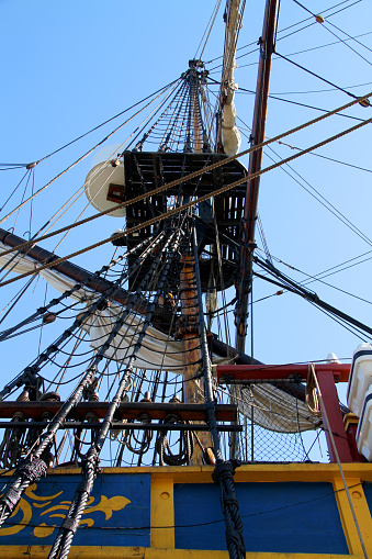 Cropped close-up detail of intricate rigging lines, sails, pulleys and hooks, rope ladders, sail booms and masts on an old, antique, tall ship sailing schooner being readied to cast off and sail at sea.