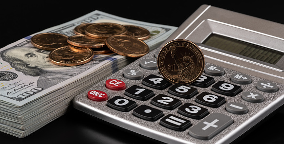 American coins and banknotes next to a calculator on a black background