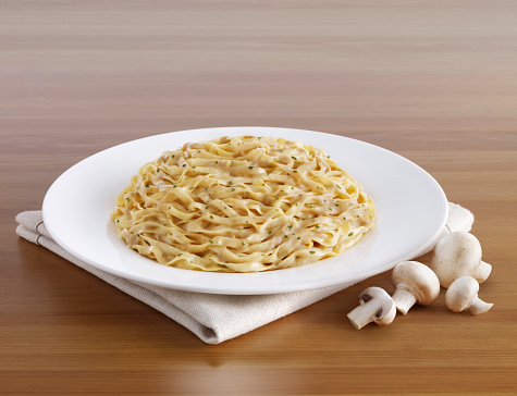 Forkful of delicious pasta in front of a pasta plate and mushrooms on a wooden table