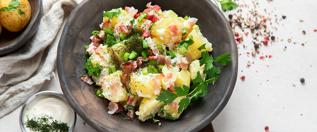 Bowl of warm potato salad with bacon on a white background. Top view. Panorama, banner.
